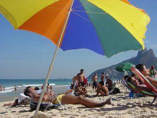 Sunbathers on the beach under a rainbow colored umbrella