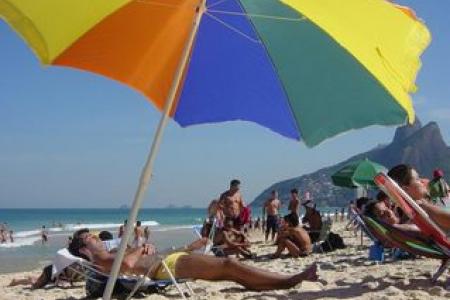 Sunbathers on the beach under a rainbow colored umbrella